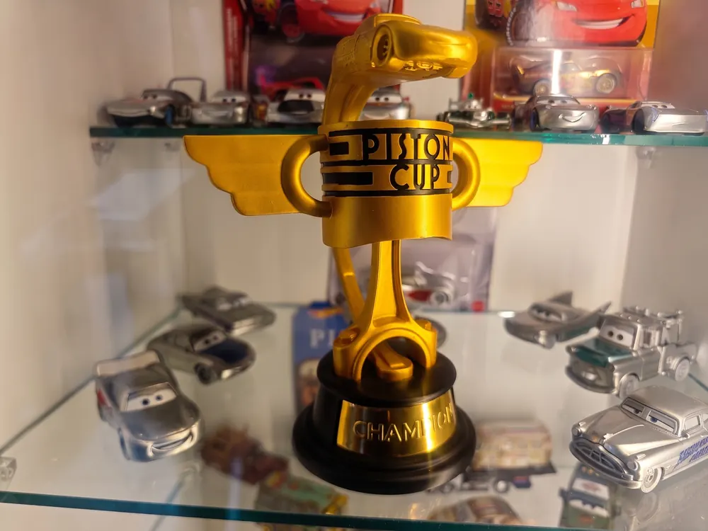 Copa Pistón dorada sobre una repisa de cristal rodeada de coches
